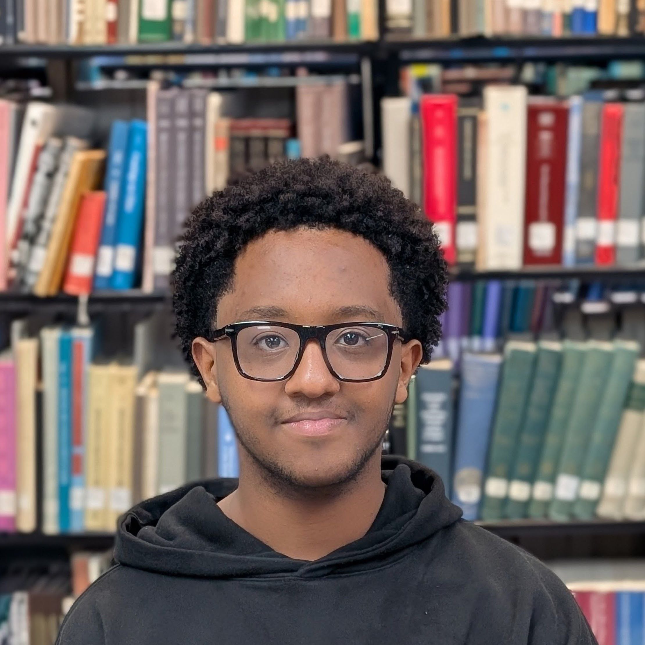 Dagim is posing in front of a bookcase 